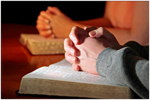 deux personnes les mains jointes en prière reposant sur leurs Bibles, posées sur une table