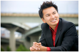 Homme de type asiatique souriant, vêtu d’un costume noir sur une chemise rouge.