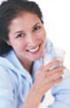 santé – femme souriante, en chemise bleue, buvant un verre d’eau